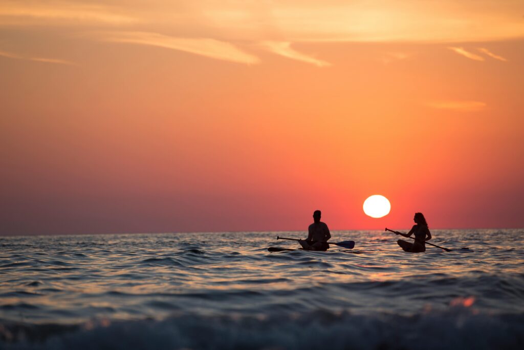 Silhouette of a couple paddleboarding on the ocean during a stunning sunset, capturing romance and adventure.