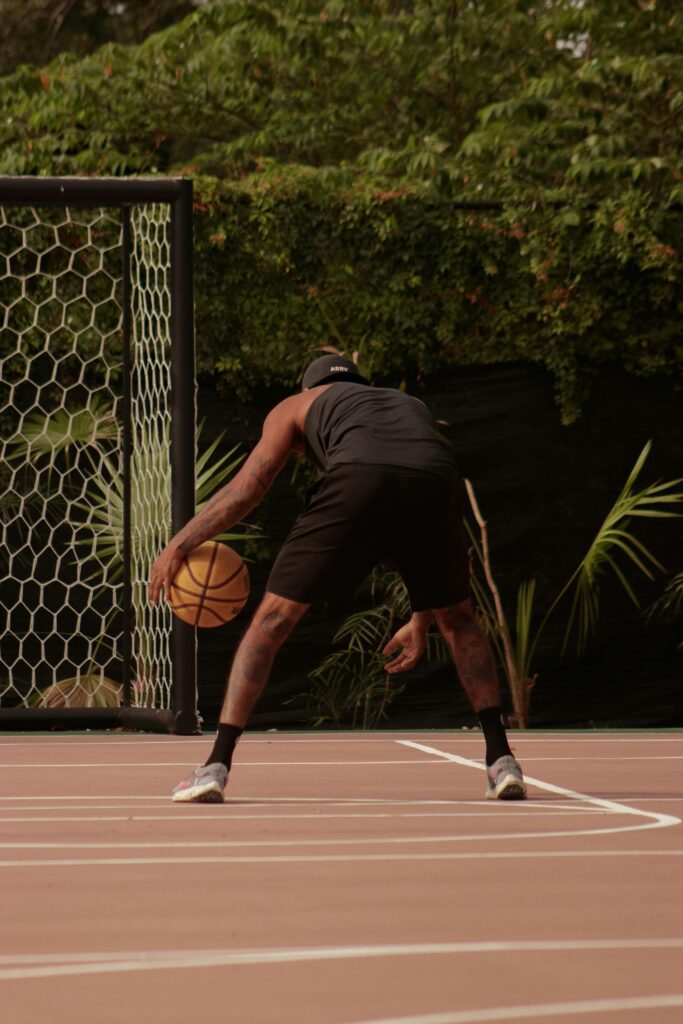 Athlete dribbling basketball on court surrounded by lush greenery.