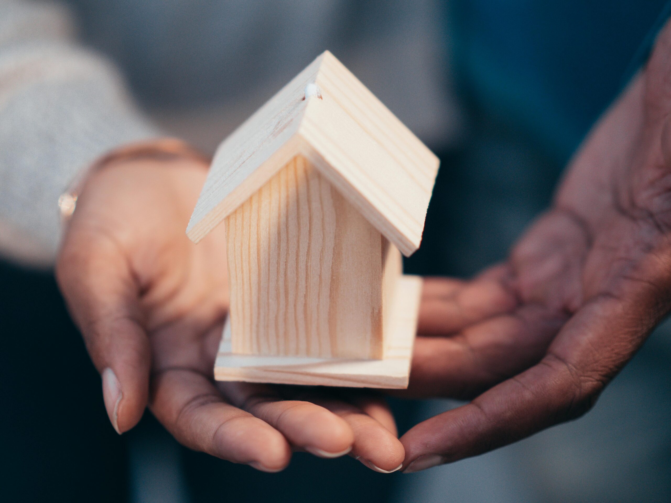 Close-up of hands holding a wooden house model representing real estate or new home purchase.