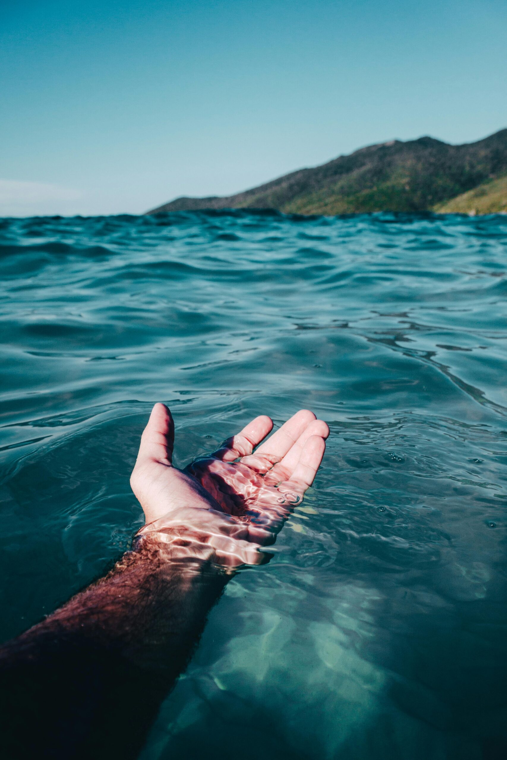 A serene hand emerges from the vibrant ocean waves at Arraial do Cabo under daylight.