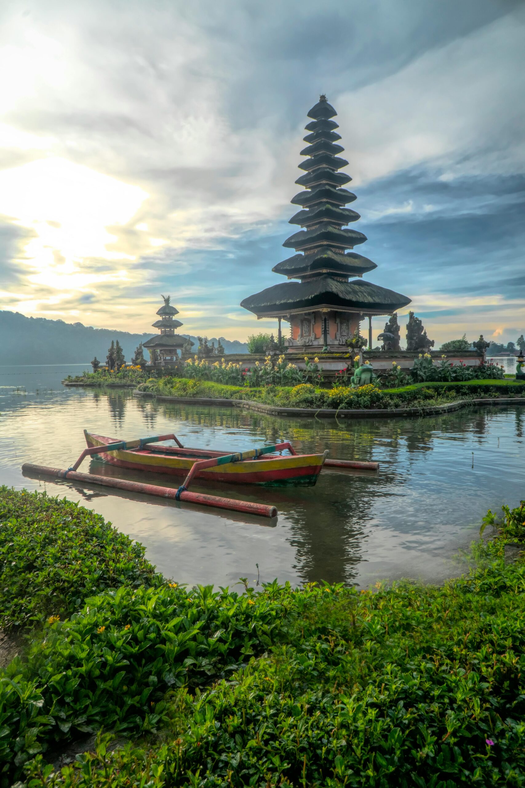 Scenic view of Ulun Danu Beratan Temple with boats on Bratan Lake, Bali at dawn.