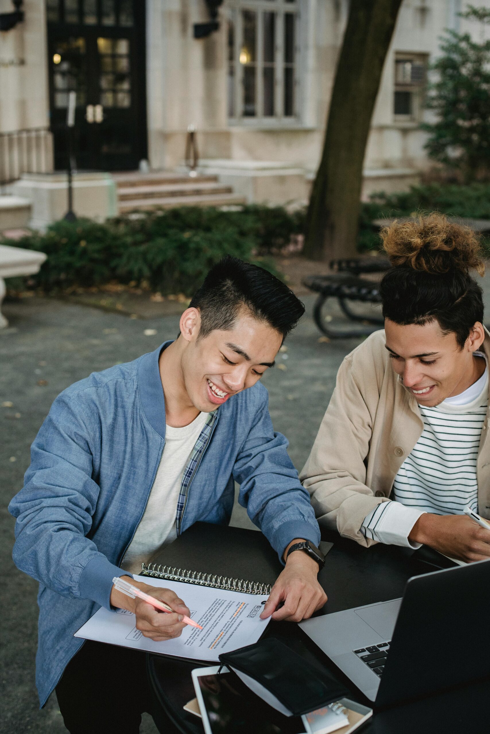 Two college students studying and discussing notes outdoors, smiling and engaged.