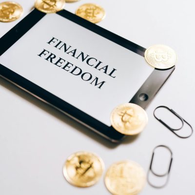 Coins are scattered around a digital tablet displaying 'Financial Freedom', symbolizing cryptocurrency wealth.